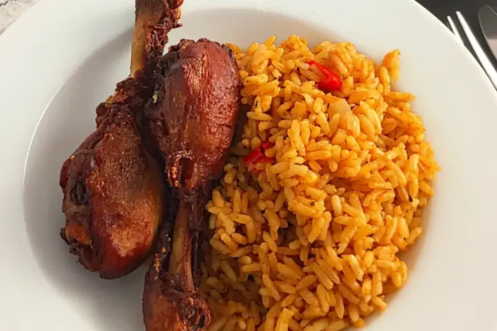 A plate of jollof rice with two fried chicken drumsticks